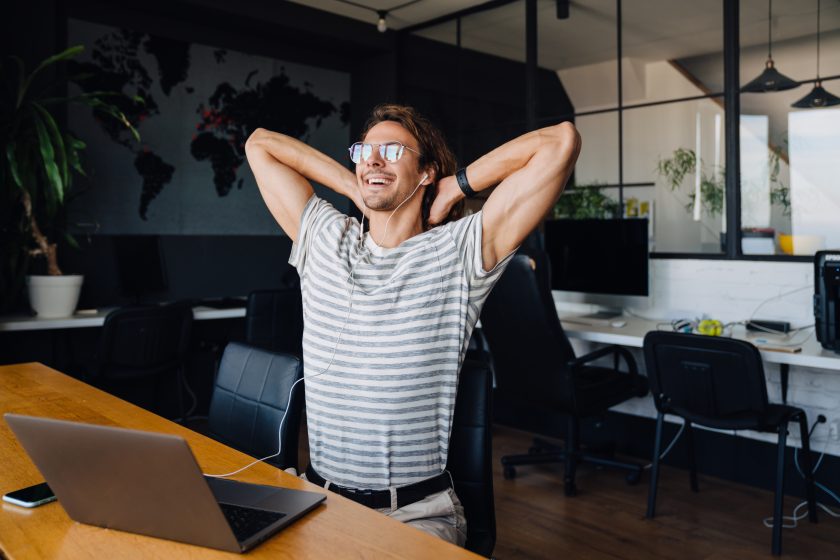 Mann mit Brille streckt sich am Schreibtisch vor Notebook